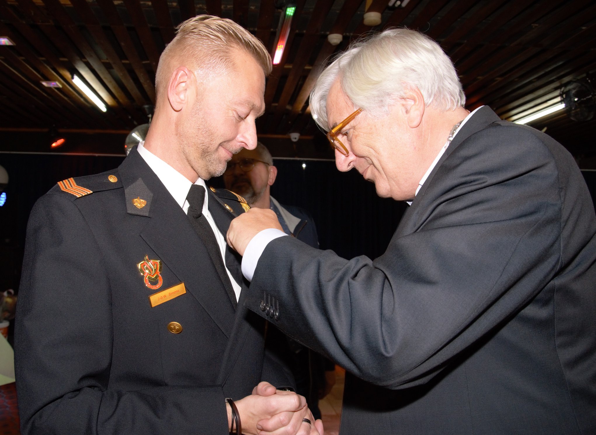 Joost Simons krijgt de Koninklijke Onderscheiding opgespeld door waarnemend burgemeester Wil Rutten